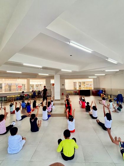 This is what a full class looks like. I guide a large group of children through seated stretches, ensuring everyone participates and learns together.