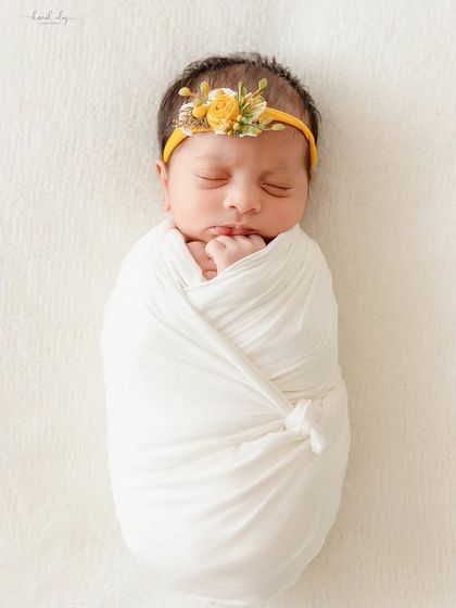 A newborn wrapped in a simple white swaddle wears a yellow floral headband, showing how minimal props can create a beautiful portrait.