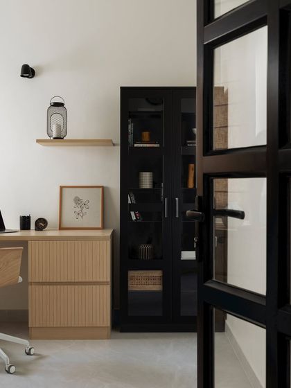 This study-cum-office space is tailored for productivity with a minimalist Japandi color scheme. A sleek black cabinet with glass shutters contrasts beautifully with the light wood desk and fluted drawers.