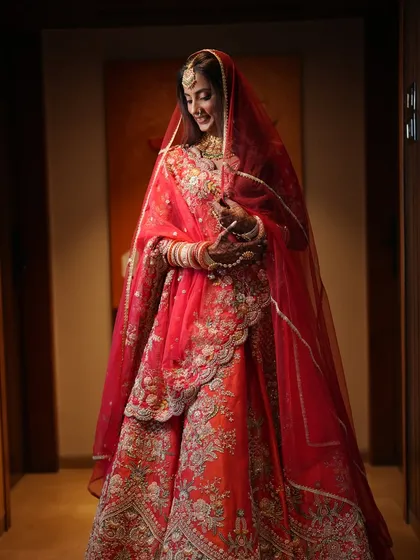 Bridal beauty that turns heads and steals hearts. This full-length shot captures the bride in a moment of quiet reflection, her red lehenga and soft makeup creating a dreamy picture.