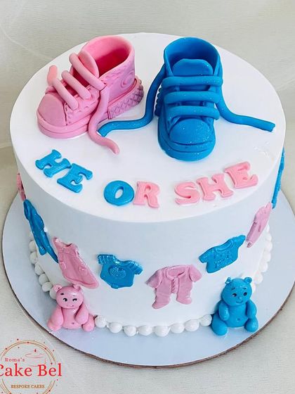 He or She? A classic gender reveal cake for a baby shower. The design features adorable pink and blue fondant baby shoes, clothes, and teddy bears, building excitement for the big reveal.