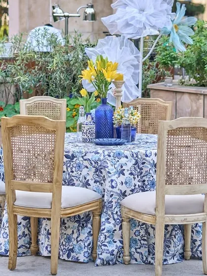 Another poolside table, this one surrounded by lush greenery, with a blue and white printed tablecloth and a vase of yellow lilies.
