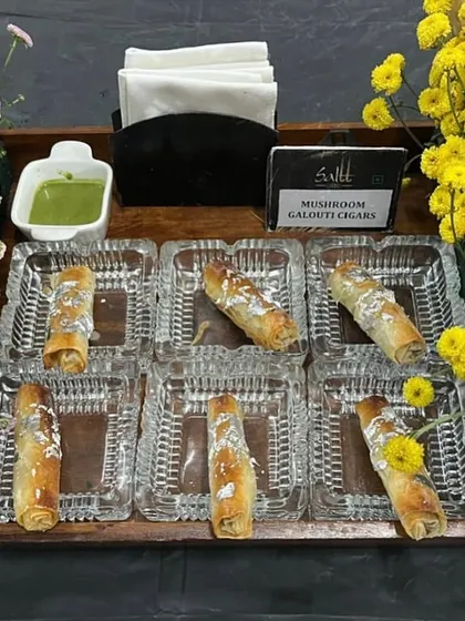 An elegant tray of Mushroom Galouti Cigars, delicately wrapped and garnished with silver varq. Served in crystal-clear dishes and surrounded by fresh flowers, this appetizer is a picture of sophistication.