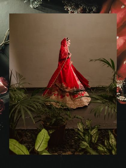 A full-length bridal portrait of Isha, surrounded by lush greenery. The contrast between her vibrant red lehenga and the natural elements creates a stunning and unique visual.