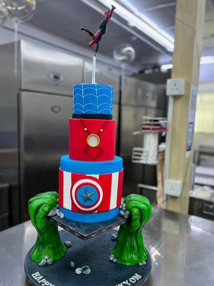 A static shot of the incredible anti-gravity Avengers cake. Held up by the Hulk's hands, this cake features tiers dedicated to Captain America, Iron Man, and Spider-Man, showcasing complex sculpting and design.