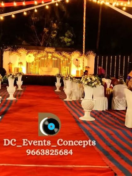 A view down the red carpet aisle, lined with floral arrangements on pedestals, leading towards the beautifully lit stage.