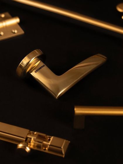 A collection of our contemporary hardware in a Gold Satin finish. This image displays the Poncho Door Lever, Norton Cabinet Pull, Royal Tower Bolt, and Hetit Cabinet Knob, showing how a complete, modern hardware solution can be achieved.