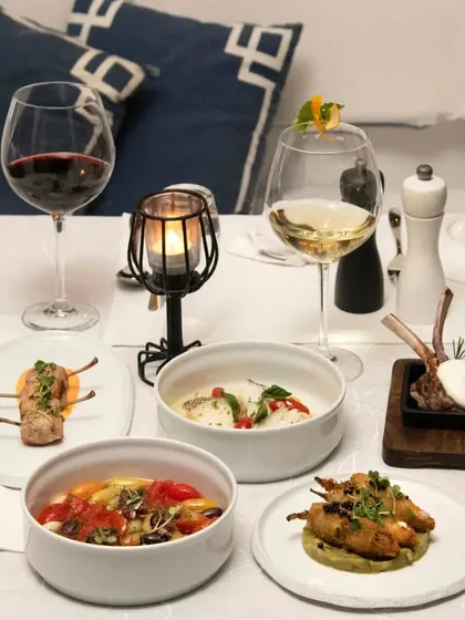 A beautiful spread of our small plates, featuring lamb chops, fish in a creamy sauce, and a vibrant tomato salad, ideal for a tasting experience.