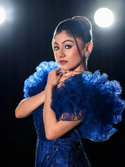 A dramatic, high-fashion look with a ruffled blue gown and bold eye makeup, created for a portfolio shoot.