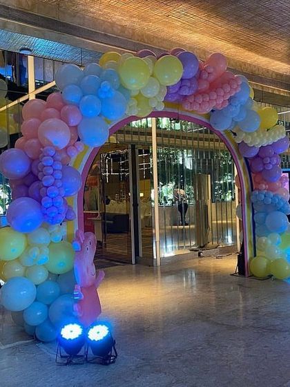 The rainbow balloon arch entrance lit up with blue spotlights, creating a magical entryway for the Peppa Pig party.