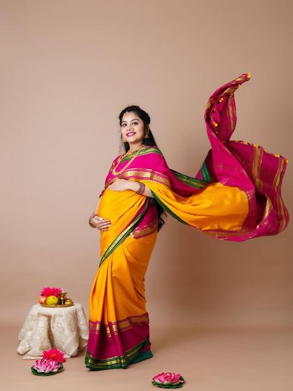 A dynamic shot of a mother-to-be in a vibrant yellow and pink saree, with the fabric flowing gracefully in the air.