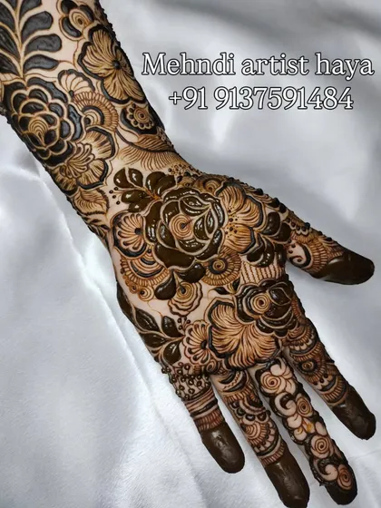 A close-up on the palm, showing the rich detail of a floral bridal design. The central rose is a masterpiece of shading and fine lines.