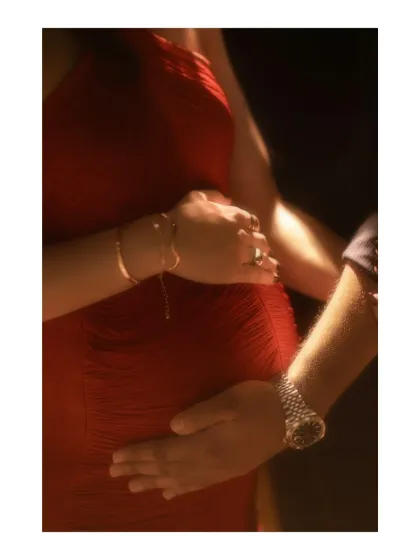 The details of connection. This tight crop focuses on the parents' hands gently holding the baby bump, a simple yet powerful image of love and protection, enhanced by warm studio lighting.