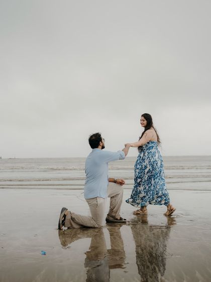 He gets down on one knee again, a playful and romantic gesture on the beach. Their reflections in the water add a touch of magic to the scene.