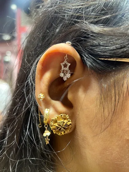 A mix of gold and silver elements creates a unique look. This ear features a hanging star piece, a large gold floral stud, and a delicate helix hanging.