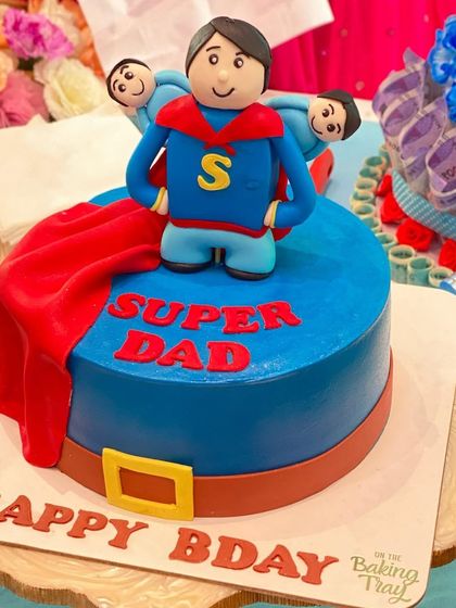 For the super dad in your life! This Superman-themed cake features a handcrafted topper of a dad with his two kids, showing he's a hero every day.