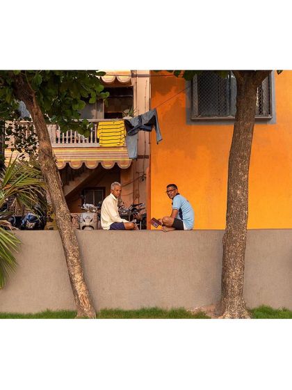 The boundary wall of a public ground can become an informal social space. Here, residents of the Worli Fishing Village gather, framed by the vibrant colors of their homes, showing how landscape architecture integrates into the existing social fabric.