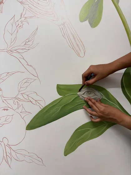 The process of integrating the pre-made clay eye into the painted leaf of a mural. This combines sculptural and painterly techniques.
