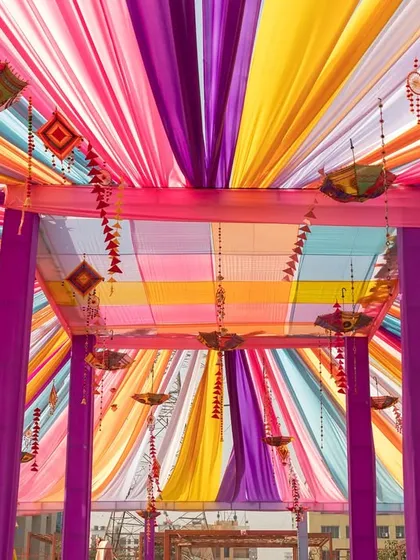 A canopy of colorful drapes creates a festive ceiling for this Haldi event. I use overhead decor to transform large spaces and create an immersive, celebratory atmosphere.