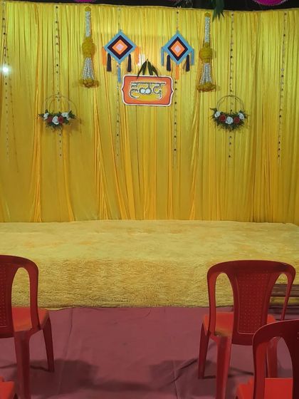 A simple Haldi backdrop with a 'Haldi' sign in Hindi. The yellow carpeted stage is ready for the ceremony.