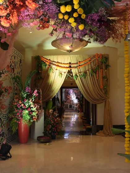 Looking through the vibrant floral archway into the event space. The path is framed by marigold garlands and traditional bells, creating a beautiful and culturally rich transition for guests.