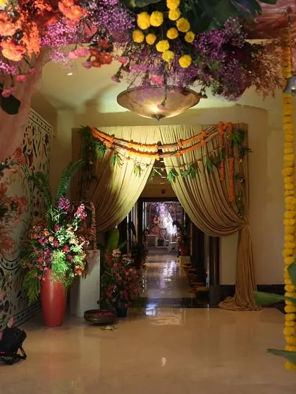 Looking through the vibrant floral archway into the event space. The path is framed by marigold garlands and traditional bells, creating a beautiful and culturally rich transition for guests.