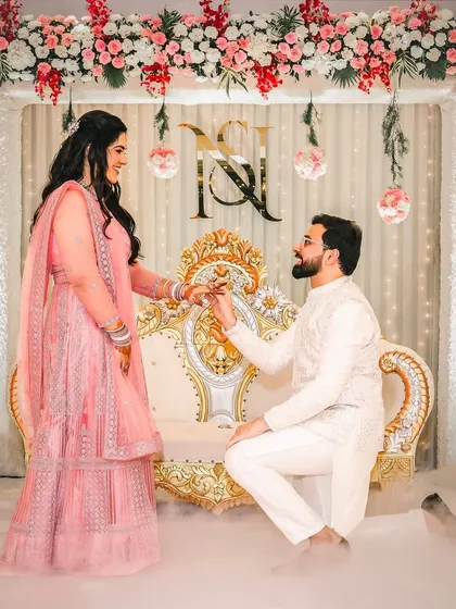 The groom gets down on one knee to offer the ring, surrounded by ethereal smoke and a beautiful floral backdrop. This is the pivotal moment of the engagement ceremony, captured with all its emotion and grandeur.