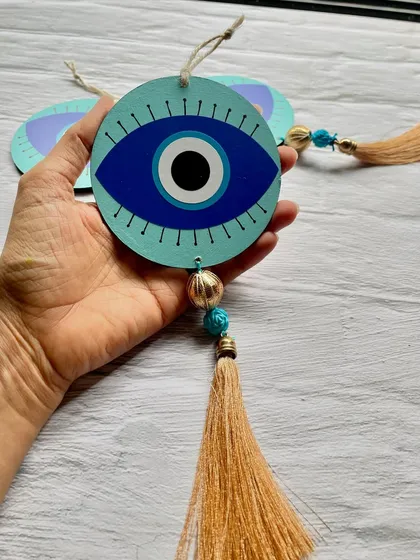 Holding one of the evil eye hangings to show its size and the detail of the tassel and beads.