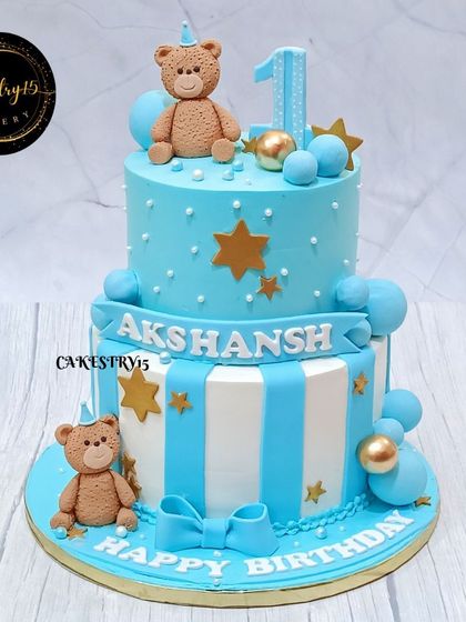 A classic teddy bear cake for a first birthday. This two-tier cake is decorated in blue and white stripes, with cute fondant teddies and golden star accents.