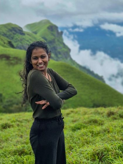A smiling trekker with the beautiful, cloud-kissed peaks of the Bandaje trail behind her.