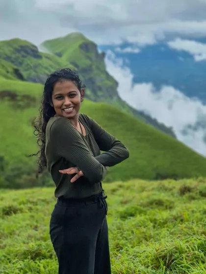 A smiling trekker with the beautiful, cloud-kissed peaks of the Bandaje trail behind her.