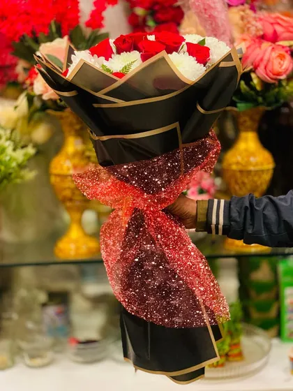 A side view of the red rose and white chrysanthemum bouquet. The black wrapping is tied with a sparkling red ribbon, making it perfect for a festive occasion.