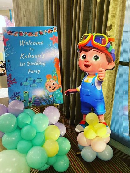 A welcome stand for a Cocomelon party, featuring a custom sign and a JJ character cutout, surrounded by pastel balloons.