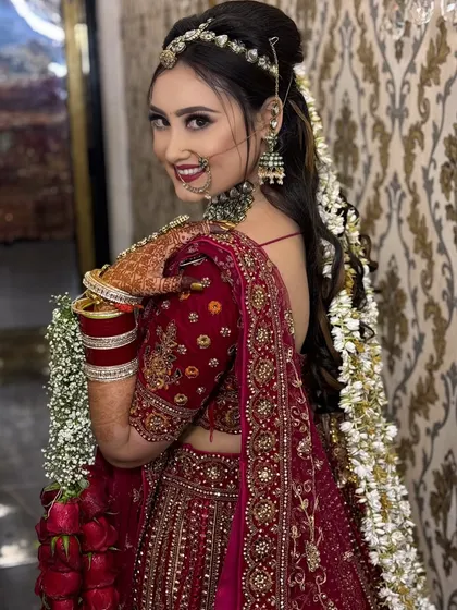 A happy bride, ready for her big day. This over-the-shoulder shot showcases her beautiful smile, flawless makeup, and the intricate details of her red lehenga and floral hair accessories.