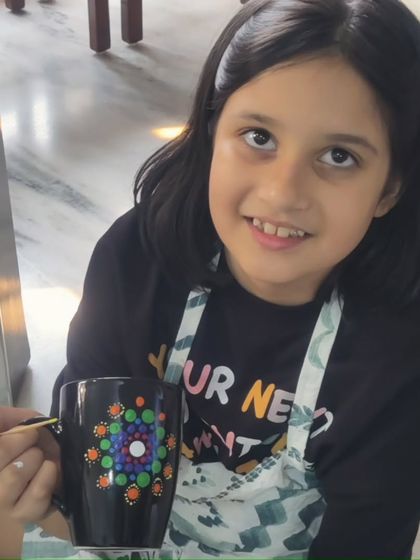 A young girl smiles while holding her finished dot mandala mug, a perfect memento from a friend's birthday.