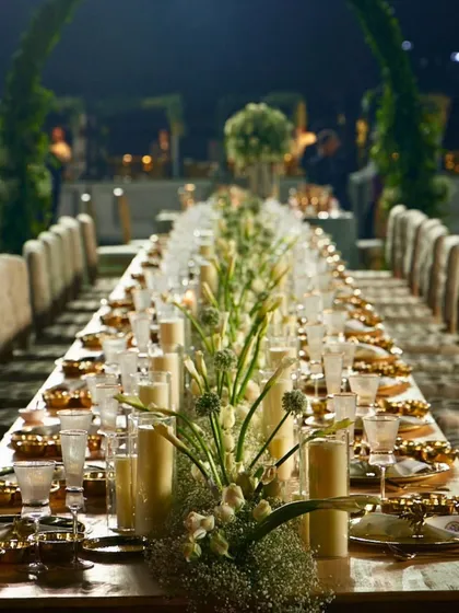 A closer look at the intimate ambiance created by our long table designs. The combination of tall pillar candles and delicate floral arrangements provides a warm, inviting atmosphere for guests to connect.