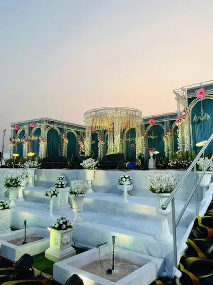 A closer look at the stage details, including the pristine white floral arrangements in classic urns, the small fountains, and the intricate design of the teal backdrops. Every element contributes to the royal theme.
