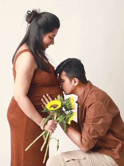 A tender kiss on the baby bump, with the mom to be holding sunflowers. Using props like fresh flowers can add a touch of natural beauty and symbolism to your couple's maternity shoot.