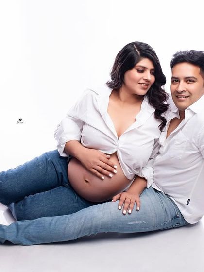 A relaxed and intimate moment between partners, both dressed in casual white shirts and jeans. This floor pose creates a comfortable and authentic connection, perfect for a lifestyle maternity session.