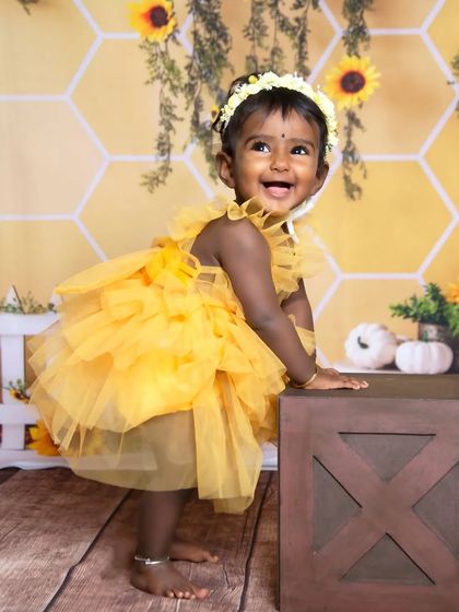 This toddler is standing and laughing, showing off her playful side during the sunflower photoshoot.