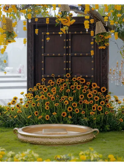 The stunning Haldi ceremony setup, featuring a traditional wooden door, a field of sunflowers, and a brass vessel, all ready for the celebration.