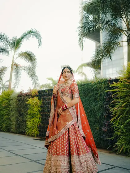 A full length bridal portrait set against a lush green backdrop. This shot showcases the bride's entire ensemble and her confident, regal posture.