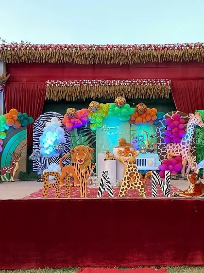 I can transform any large outdoor space, like this farmhouse lawn, into a vibrant jungle. This setup features a massive stage with life-sized animal props like elephants and giraffes, themed backdrops, and colorful balloon arrangements to create an immersive safari experience for a child's birthday.