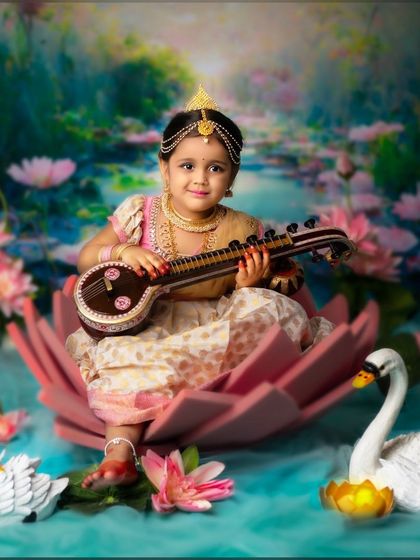 A beautiful little girl dressed as Goddess Saraswati, sitting in a lotus and holding a mini veena.