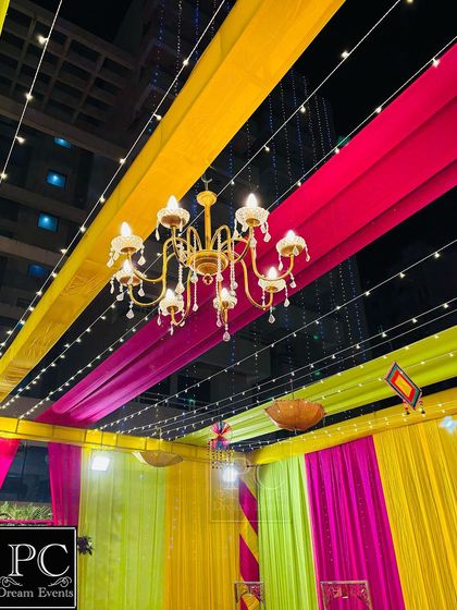 A detail shot of the ceiling decor, showing the combination of colorful fabric strips, fairy lights, and a classic chandelier that illuminates the entire space.