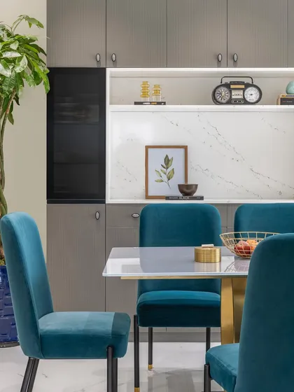 The dining area exudes elegance with its subtle shade of blue in the velvet chairs. Lush indoor plants and captivating artifacts on the built-in shelving create a charming and sophisticated ambiance for meals.