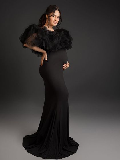 A full-length portrait showing the dramatic silhouette of the black ruffled gown.
