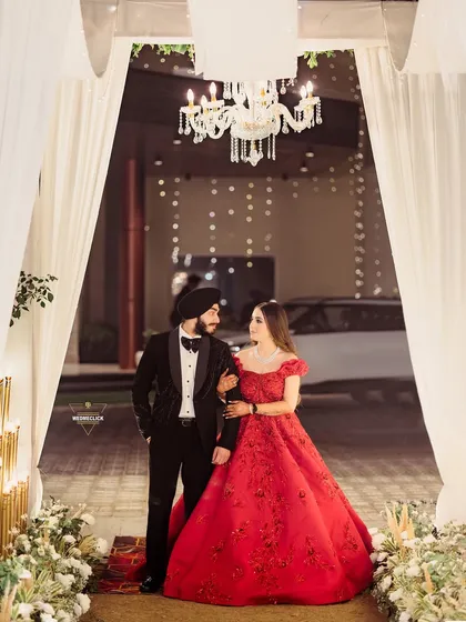 Making a grand entrance. The combination of the stunning red gown, the classic tuxedo, and the elegant decor with its warm chandelier light creates a feeling of pure glamour. I work to compose shots that are not just photos, but timeless statements of style and love.