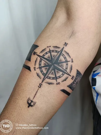 A travel-themed armband tattoo featuring a compass. The compass points are integrated into a geometric band, symbolizing a love for adventure and always finding your own direction.