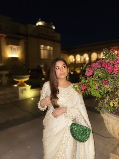 An elegant white saree is a timeless choice for any wedding event. Here, I've paired it with a contrasting green bag for a pop of color, creating a sophisticated look for an evening celebration.